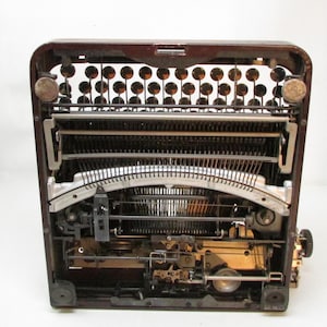 May include: A vintage typewriter with a dark brown exterior. The internal mechanisms, including the keys, levers, and typebars, are visible. The typewriter has a classic design, with round keys and a carriage return lever.
