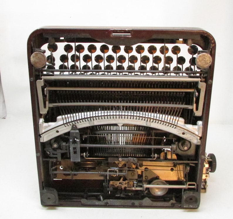 May include: A vintage typewriter with a dark brown exterior. The internal mechanisms, including the keys, levers, and typebars, are visible. The typewriter has a classic design, with round keys and a carriage return lever.