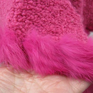 May include: Close-up of a vibrant pink garment with a textured, fuzzy fabric. The bottom edge is trimmed with a band of bright pink, fluffy fur. The garment's color is a bold, eye-catching hue.