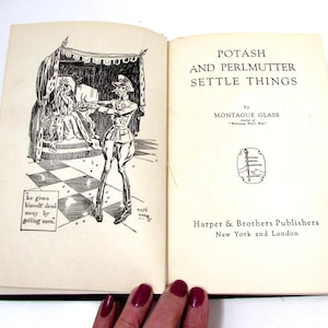 Pode incluir: Livro aberto intitulado "Potash and Perlmutter Settle Things" de Montague Glass. As páginas do livro exibem uma ilustração em preto e branco de um homem apontando uma arma para uma pessoa na cama. Publicado por Harper & Brothers Publishers.