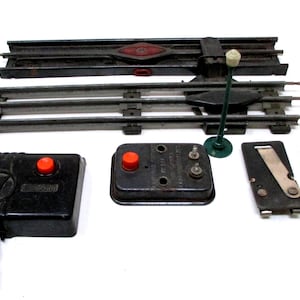 May include: Vintage model train set components, including black track, a signal, and control boxes with red buttons. The set includes a "Lionel CTC Lockon" piece.