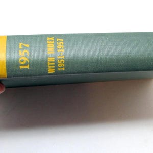 Könnte beinhalten: Ein Vintage-Buch mit dem Titel "Current Biography 1957" mit einem Index, der die Jahre 1951-1957 abdeckt. Das Buch hat einen teal-farbenen Einband mit gelben Bändern und Text. Der Buchrücken zeigt den Namen des Verlags und eine Bibliotheksnummer.
