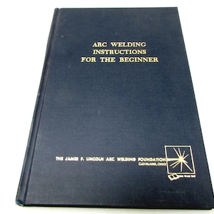 May include: A dark blue hardback book titled ARC WELDING INSTRUCTIONS FOR THE BEGINNER in gold lettering. The cover features the text THE JAMES F. LINCOLN ARC WELDING FOUNDATION CLEVELAND, OHIO and a gold graphic logo in the bottom right corner.