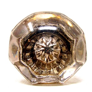 Puede incluir: Un pomo de puerta antiguo de cristal transparente, con forma octogonal y un diseño detallado en forma de estrella en el centro. El cristal tiene una calidad ligeramente iridiscente, que refleja la luz. Un elemento decorativo para puertas.