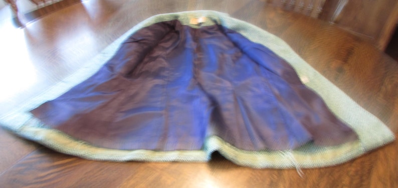 May include: A light green textured coat with a dark blue interior lining. The garment features a collar and long sleeves, with the front open to reveal the smooth, dark blue fabric inside. The outer material has a visible woven pattern.