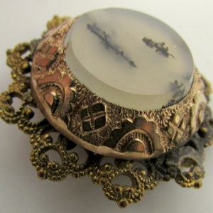 May include: A vintage brooch with a delicate gold filigree design and a round, white agate stone with black and gray inclusions.