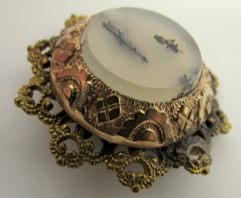 May include: A vintage brooch with a delicate gold filigree design and a round, white agate stone with black and gray inclusions.