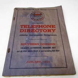 May include: A vintage January 1915 Alberta Government Official Telephone Directory for the Southern Division. The light purple paper cover features red and black text, a circular government emblem, and lists Calgary, Lethbridge, and Medicine Hat.