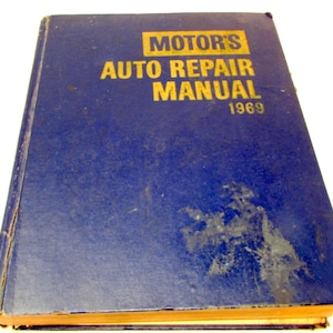 Op de afbeelding: Een vintage blauwe Motor's Auto Repair Manual uit 1969. Het boek heeft gouden letters en een versleten kaft. De randen van het boek zijn vergeeld door ouderdom, wat aangeeft dat het een oudere publicatie is. De handleiding is waarschijnlijk voor autoreparatie.
