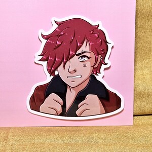 May include: A sticker featuring a stylized illustration of a character with red hair and a determined expression. The character wears a red jacket with a black collar and has a tattoo on their face. The sticker is on a pink background.
