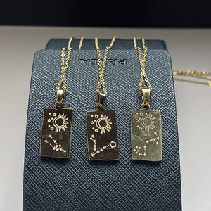 May include: Three gold necklaces with rectangular pendants featuring a crescent moon, sun, and stars design. Each pendant has a constellation design.