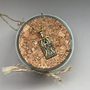 May include: Gold necklace with a pendant featuring a black and white illustration of a tarot card with the word "Taurus" on it.