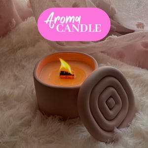 Pode incluir: Uma vela de cerâmica rosa com tampa. A vela está acesa e a chama é visível. A tampa tem um design em espiral.