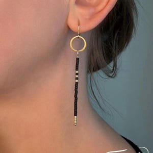 May include: Gold hoop earrings with a long black beaded dangle. The beads are black with gold accents.