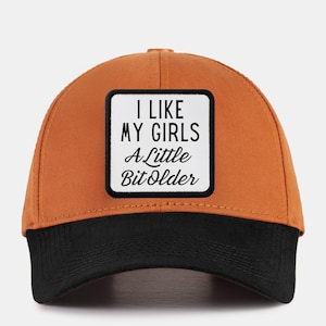 Peut inclure: Une casquette de baseball marron et noire avec un patch blanc qui dit "J'aime mes filles un peu plus âgées".