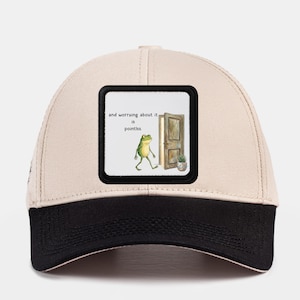 May include: A white ceramic mug with a black handle and the text "But First, Coffee" in a bold, black font. The mug is set against a blurred background. The mug appears to be approximately 10 cm tall.