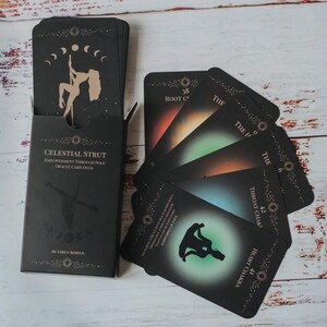 May include: A black oracle card deck titled "Celestial Strut" with a silhouette of a person pole dancing. The cards are fanned out, displaying colorful chakra-themed illustrations. The deck includes the text "Empowerment Through Pole Oracle Card Deck."