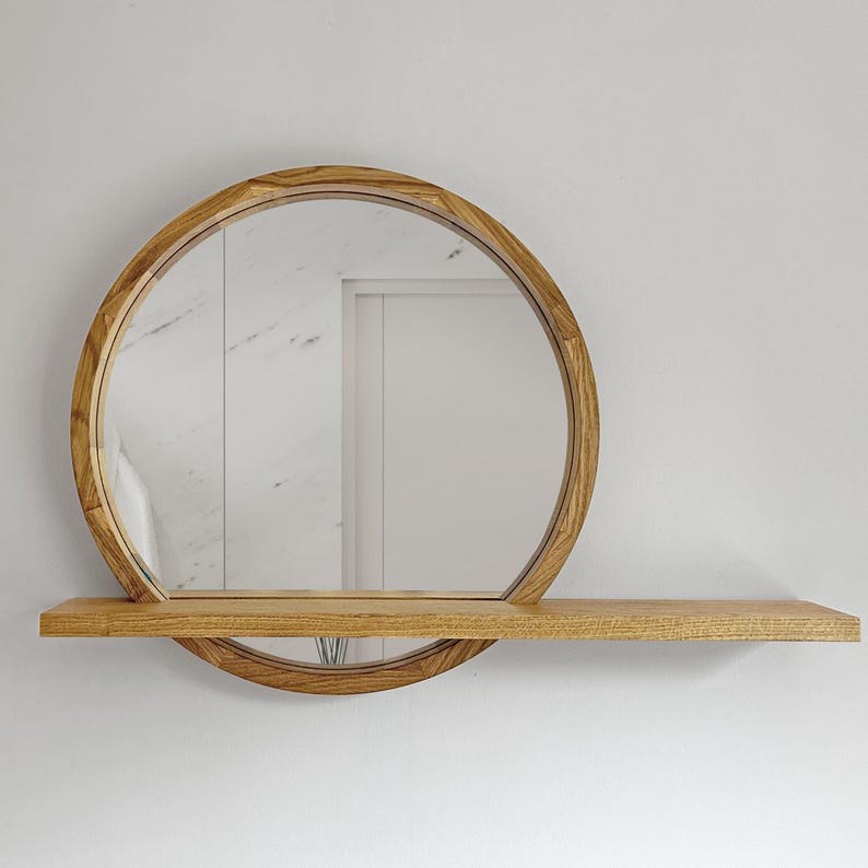 May include: A round wooden mirror with a shelf. The mirror has a natural wood finish and a decorative geometric pattern around the edge. The shelf is rectangular and extends horizontally from the mirror's base.