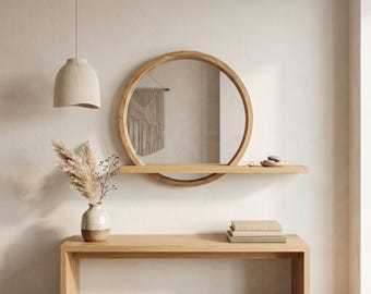 May include: A circular wooden mirror with an integrated horizontal shelf, mounted on a wall above a wooden console table. The mirror frame is light brown wood, and the shelf holds small decorative stones. A vase with dried grass sits nearby.