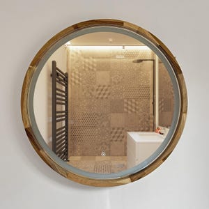 May include: Round wooden-framed mirror with a mosaic-style border. The mirror has a built-in light and is mounted on a white wall. The reflection shows a bathroom with patterned tiles and a white vanity.