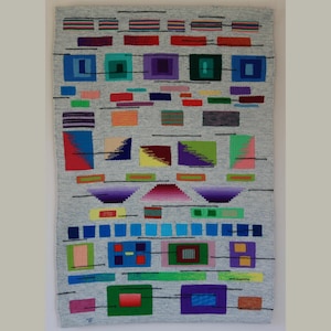 May include: A gray woven wall hanging with a geometric design. The design features colorful rectangular and square shapes in shades of blue, green, purple, red, and orange. Black lines connect some of the shapes. The wall hanging is rectangular.