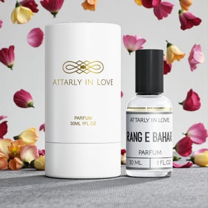 May include: A perfume bottle and its white cylindrical box are displayed against a floral background. The bottle is clear with a black cap, and the box has gold lettering that reads "ATTARLY IN LOVE" and "PARFUM 30ML 1FL.OZ.". The bottle also reads "RANG E BAHAR".