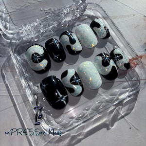 May include: A set of ten oval-shaped press-on nails with a black and white abstract design. The nails have a glittery finish and feature a star design.