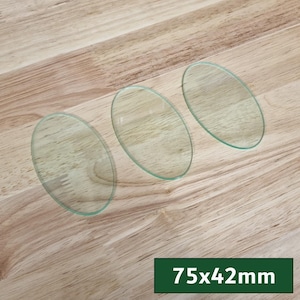 Può includere: Tre pezzi di vetro trasparente di forma ovale con una sfumatura verde sono disposti su una superficie di legno marrone chiaro. Le dimensioni sono 7,5 cm x 4,2 cm. Il vetro ha una leggera curvatura.