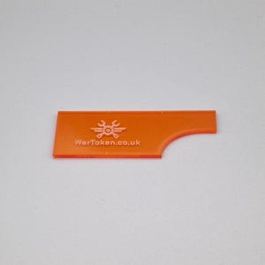 May include: An orange game accessory with a rectangular shape and a curved edge. The text "WarToken.co.uk" is printed on the surface, along with a graphic of a wrench and gears.