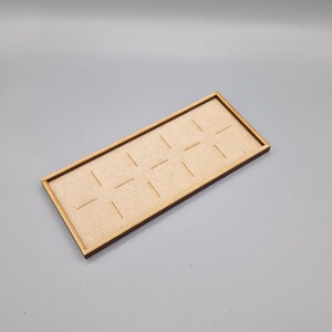 May include: A wooden tray with a rectangular shape and a light brown finish. The tray has 12 evenly spaced slots cut into the surface.