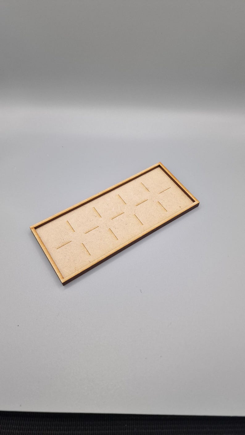 May include: A wooden tray with a rectangular shape and a light brown finish. The tray has 12 evenly spaced slots cut into the surface.