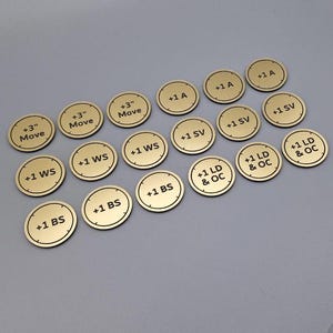 May include: A set of 18 gold-coloured round tokens with black text. The tokens feature various game stats, including +3" Move, +1 WS, +1 BS, +1 SV, +1 LD & OC, and +1 A.