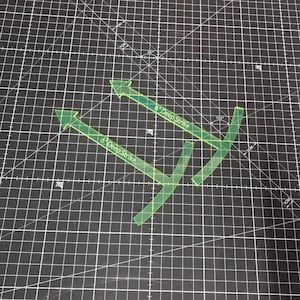 May include: A set of transparent green quilting rulers with arrow shapes and the text "6 Deep Strike". The rulers are on a black cutting mat with white grid lines, designed for precise fabric cutting and quilting projects.