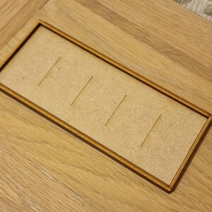 May include: A wooden tray with five slots, perfect for organizing small items. The tray is made of light brown wood and has a dark brown border.