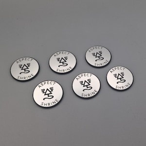 Può includere: Sei gettoni rotondi in metallo color argento con un design nero. Ogni gettone presenta un albero alato stilizzato con il testo "ASPECT SHRINE" attorno al design.