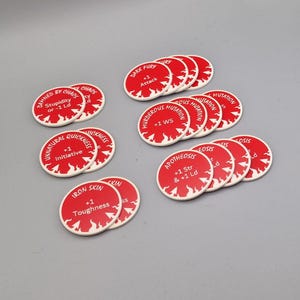 May include: A collection of 14 red and white circular tokens with white text and a flame design. The tokens have various text including "Damned by Chaos", "Unnatural Quickness", "Iron Skin", "Dark Fury", "Murderous Mutation", and "Apotheosis".