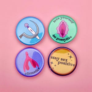 Könnte beinhalten: Vier runde Ansteckbuttons mit verschiedenen Designs und Texten. Ein Button zeigt einen Vibrator und eine Sichel, ein anderer sagt "love yourself be pussyfive", ein dritter sagt "clittastic!" und der letzte sagt "stay sex positive".