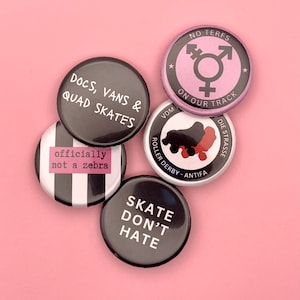 Op de afbeelding: Vijf ronde zwart-witte knoppen met verschillende berichten. De knoppen hebben een zilveren achterkant. De berichten op de knoppen zijn: "Docs, Vans & Quad Skates", "officieel geen zebra", "Skate Don't Hate", "No Terfs On Our Track" en "Vom Die Strasse Roller Derby - Antifa".