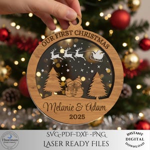 May include: A wooden Christmas ornament with the text "OUR FIRST CHRISTMAS" and the names "Melanie & Adam" with the year "2025". The ornament features a laser-cut design of reindeer, a sleigh, Christmas trees, and snowmen.