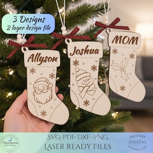 May include: Three wooden Christmas stocking ornaments with names "Allyson", "Joshua", and "MOM". Each stocking has a different design: Santa Claus, a snowman, and holly. The ornaments are decorated with snowflakes and tied with red and black plaid ribbons.