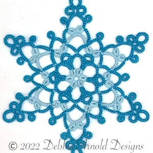 May include: A teal blue and light blue crocheted snowflake with a delicate design. © 2022 Debbie Arnold Designs