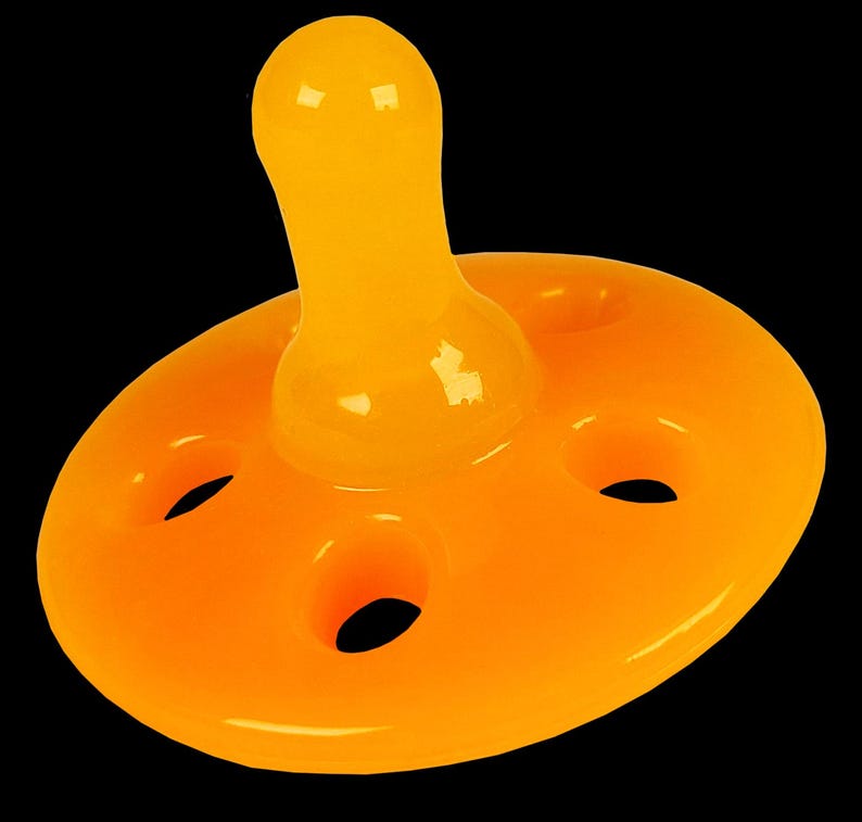 K&ouml;nnte beinhalten: Ein leuchtend orangefarbener Schnuller f&uuml;r Babys mit einer runden, flachen Basis und einem Sauger in Form eines abgerundeten Rechtecks. Die Basis hat vier L&ouml;cher am Rand.