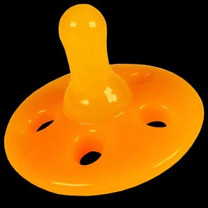 Op de afbeelding: Een feloranje baby speen met een ronde, platte basis en een tepel in de vorm van een kleine, afgeronde koepel. De basis heeft vier kleine gaatjes rond de rand.