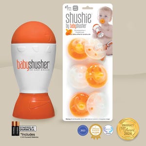 Op de afbeelding: Een oranje en witte baby shusher met een witte speen op een witte en oranje achtergrond. Het product wordt aangedreven door twee AA-batterijen. De verpakking bevat de tekst "shushie by babyshusher" en "The Sleep Miracle".