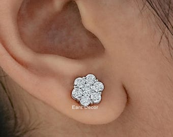 Puede incluir: Un pendiente de botón plateado con un grupo de siete pequeñas piedras transparentes de corte redondo dispuestas en forma de flor. El pendiente está colocado en un lóbulo y el texto Ears Decor aparece en letras blancas pequeñas debajo.