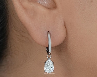 May include: A silver-toned hoop earring featuring a dangling pear-shaped clear gemstone. The earring is secured with a hinged closure. The small text "Ears Decor" is visible near the base of the gemstone setting on the metal component.