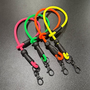 Puede incluir: Cuatro cordones de colores en rosa, verde, naranja y amarillo. Cada cordón tiene un mosquetón negro y un conector negro. Los cordones están hechos de un material flexible similar al caucho.