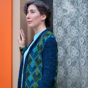 May include: A woman wearing a blue, green, and teal cardigan with a geometric pattern. The cardigan is knitted and has a shawl collar.