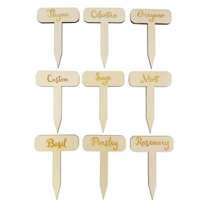 May include: Nine wooden plant markers with different herb names, including Thyme, Cilantro, Oregano, Custom, Sage, Mint, Basil, Parsley, and Rosemary. The markers are rectangular with rounded corners and have a wooden stake.