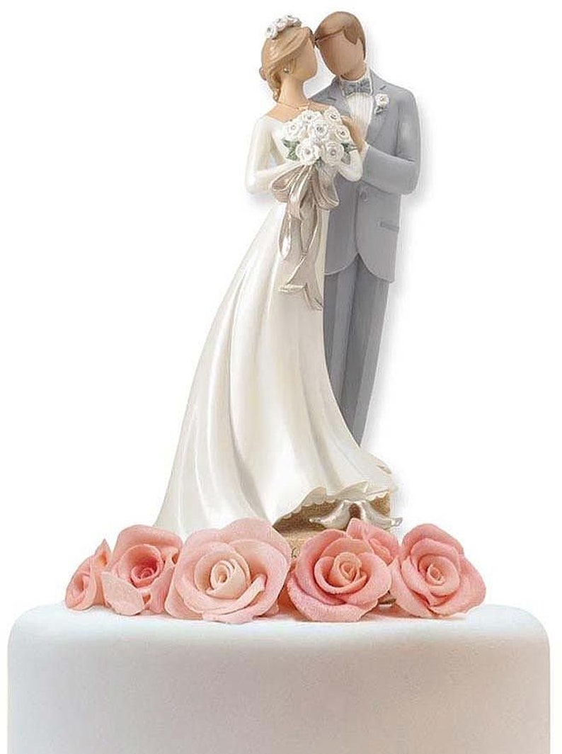 K&ouml;nnte beinhalten: Ein wei&szlig;er Hochzeitstortenaufsatz mit einer Braut- und Br&auml;utigamfigur. Die Braut tr&auml;gt ein wei&szlig;es Kleid und einen Schleier, der Br&auml;utigam einen grauen Anzug. Das Paar steht auf einem Sockel, der mit rosa Rosen verziert ist.